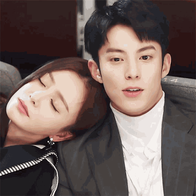 a man and a woman are posing for a picture and the woman is sleeping on the man 's shoulder